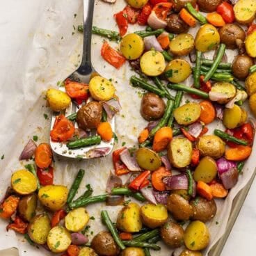 square image of roasted vegetables on a baking sheet with a metal spatula.