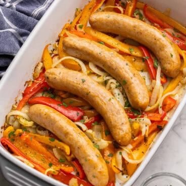 baked sausage and peppers in a white and grey baking dish.