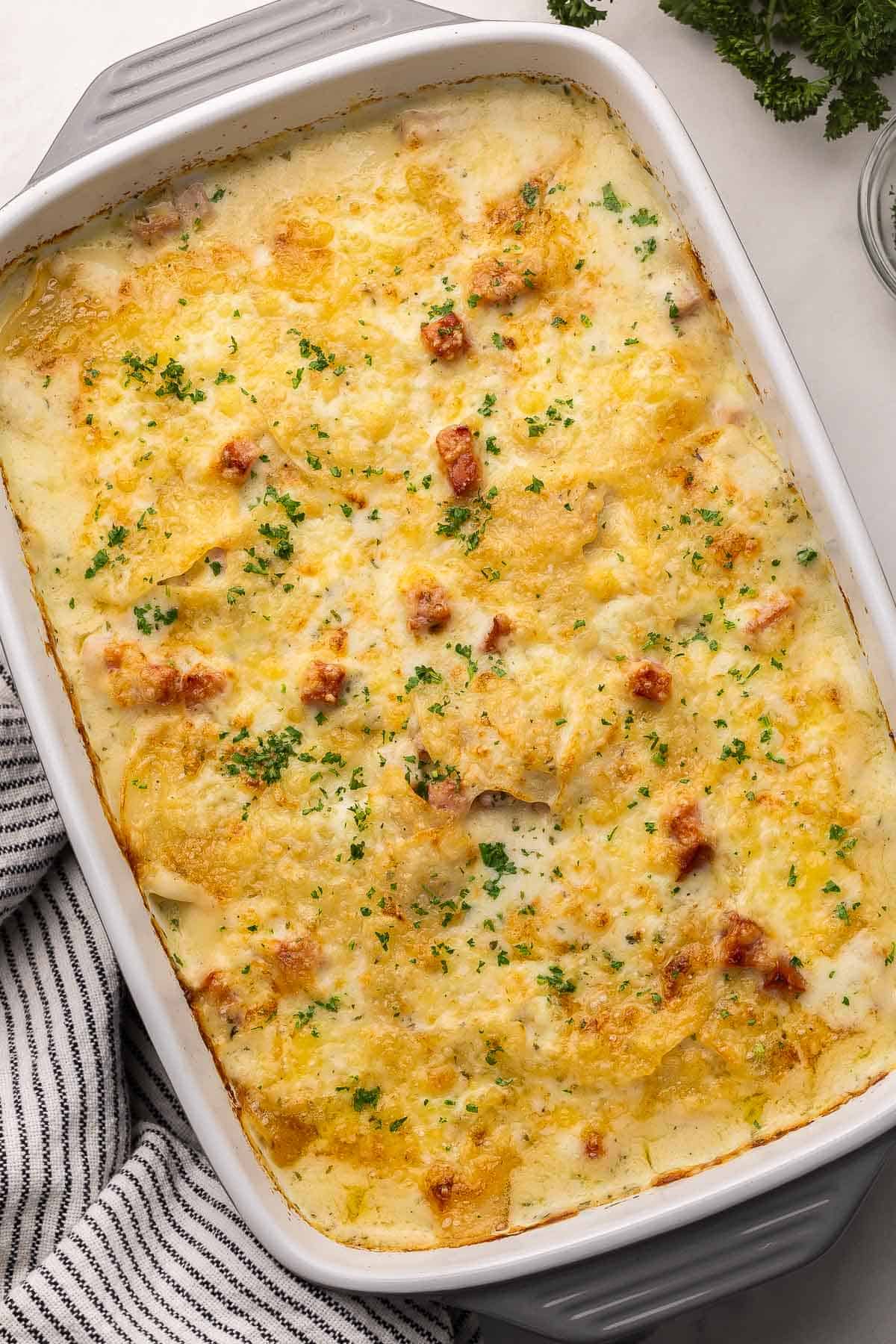 Scalloped Potatoes and Ham is a cheesy, creamy potato casserole made with layers of potatoes and ham cooked in a creamy white sauce. It's a comforting side dish perfect for a holiday meal or Sunday dinner! #dinner #recipe | potatoes | potato recipe | casserole recipe | holiday side dish | side dishes | comfort food large gray and white pan full of scalloped potatoes and ham.
