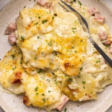 scalloped potatoes and ham on a plate with a fork in it.
