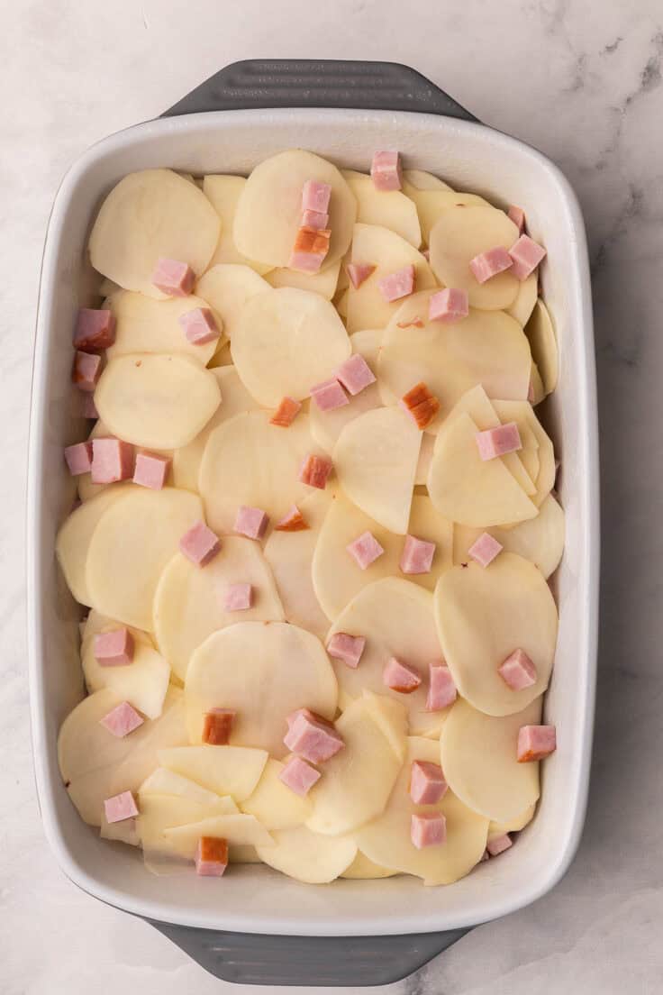 sliced potatoes laid in large baking dish topped with cubed ham.