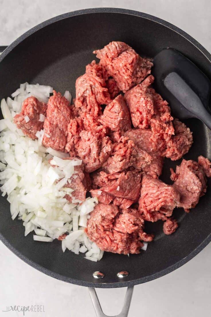 uncooked ground beef and chopped onions in black frying pan.