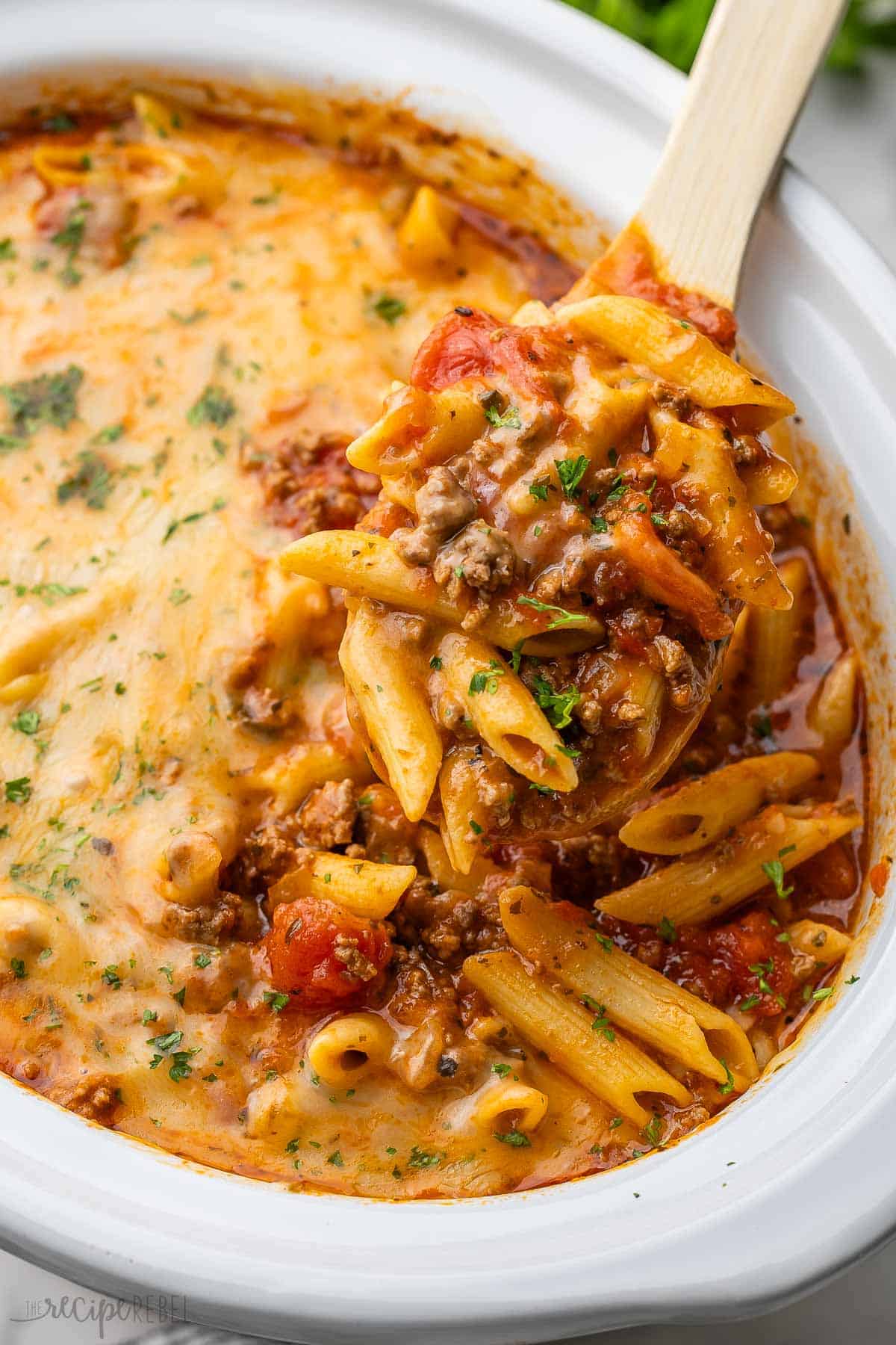 This Slow-Cooker Baked Ziti is made completely in the crockpot—even the pasta! It is so much easier than the traditional version but packs all of the same flavor! The recipe includes a step-by-step video. #recipe #dinner #slowcooker | slow cooker dinner | crockpot meals | crockpot recipes | slow cooker recipes | ground beef recipes | pasta recipe | easy dinner ideas | ground beef pasta a scoop of slow cooker baked ziti coming out of a white crockpot.