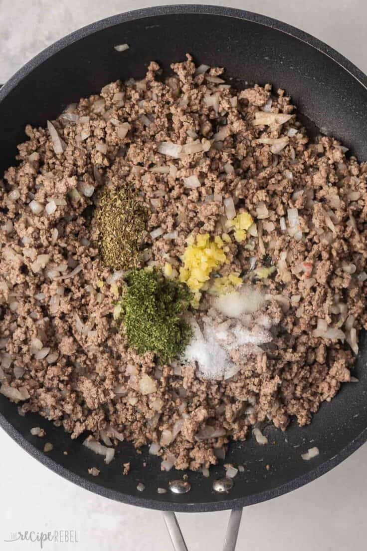 cooked ground beef and onions with spices added in pan.