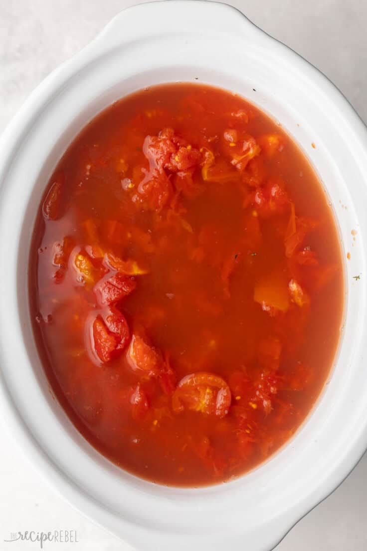 white slow cooker with diced tomatoes added.