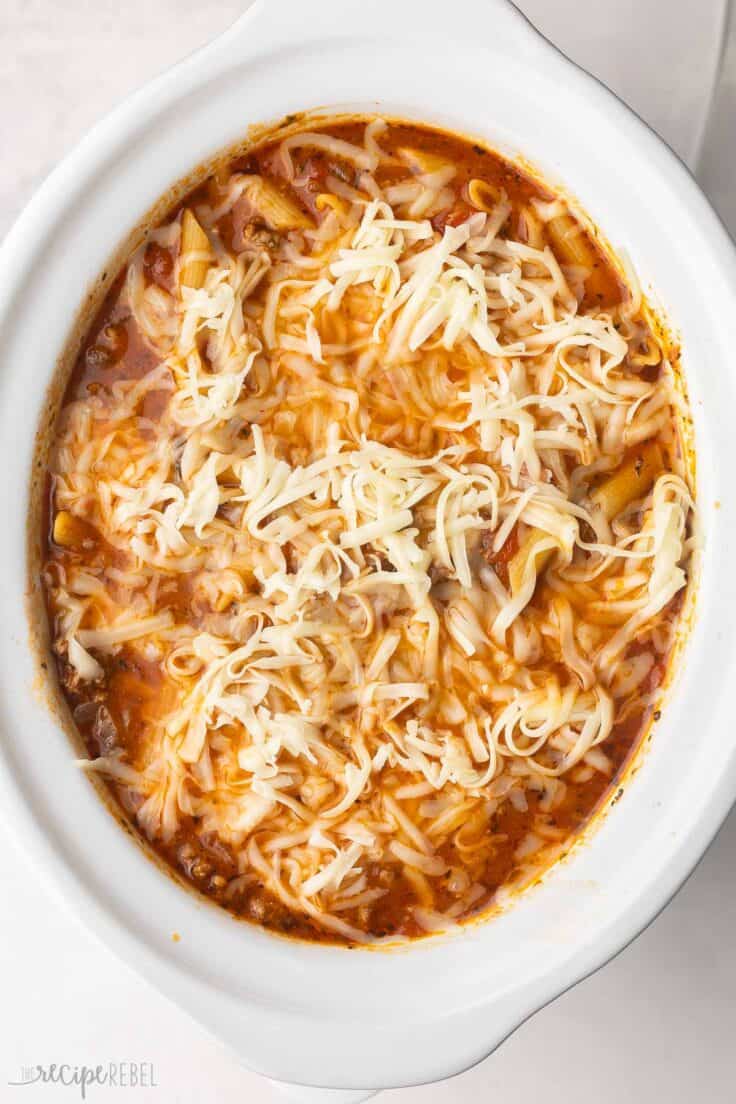 white slow cooker filled with baked ziti and shredded mozzarella on top.