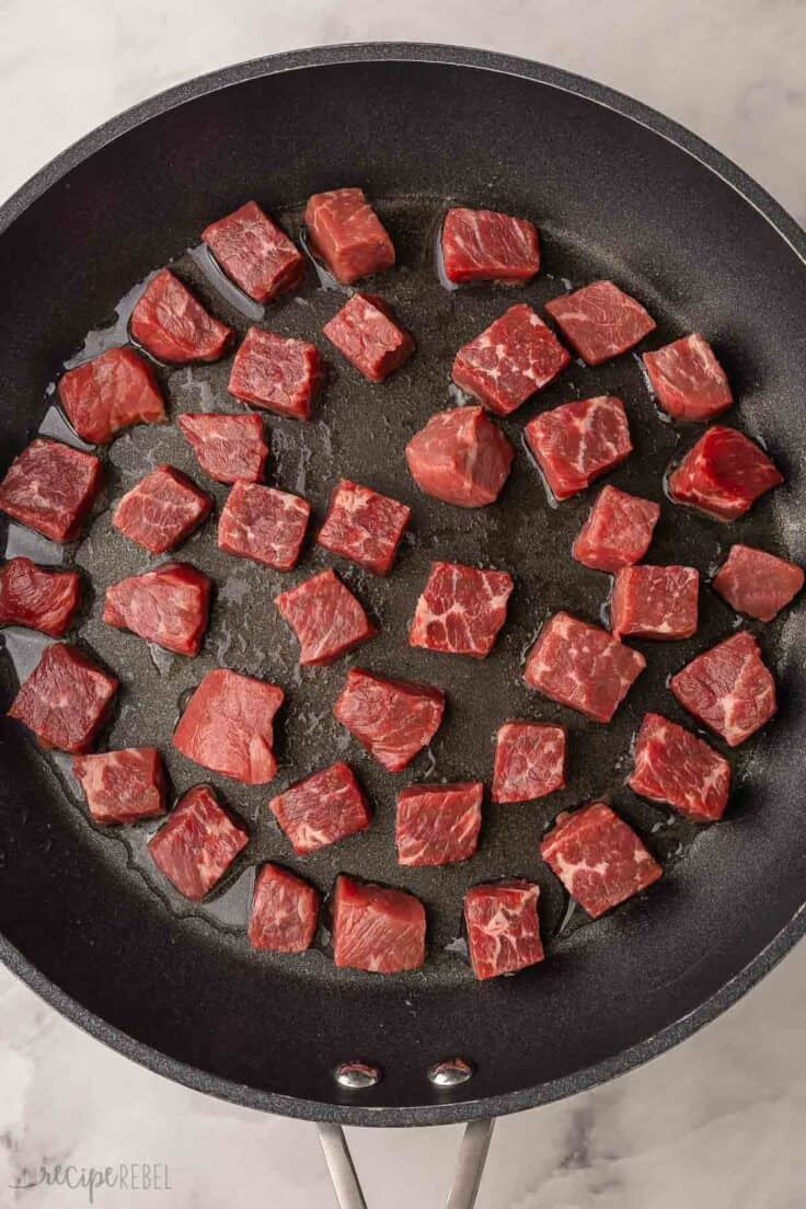 cubes of beef in black frying pan.