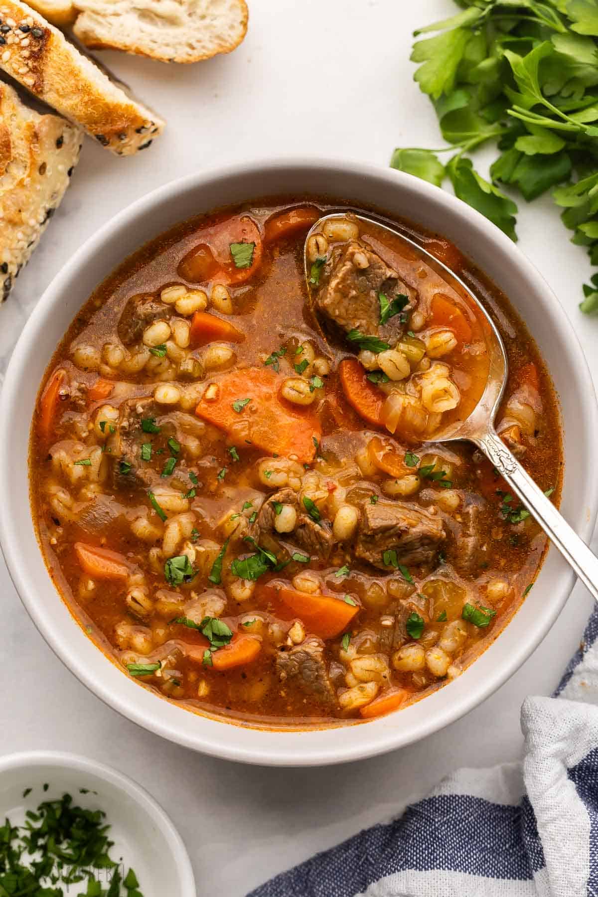 This Slow Cooker Beef Barley Soup is loaded with tender beef, barley, and vegetables simmering in a rich broth. It's the perfect crockpot meal for warming you up on a chilly day! #soup #recipe #dinner | soup recipes | beef recipes | comfort food | slow cooker soup | crockpot soups | crockpot meals | easy dinner ideas large bowl of beef barley soup with a spoon in it.