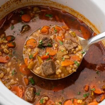 square image of a metal ladle scooping crockpot beef barley soup.