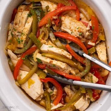 white crockpot with tongs scooping out chicken and peppers.