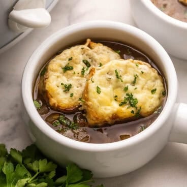french onion soup in a white bowl with parsley beside.