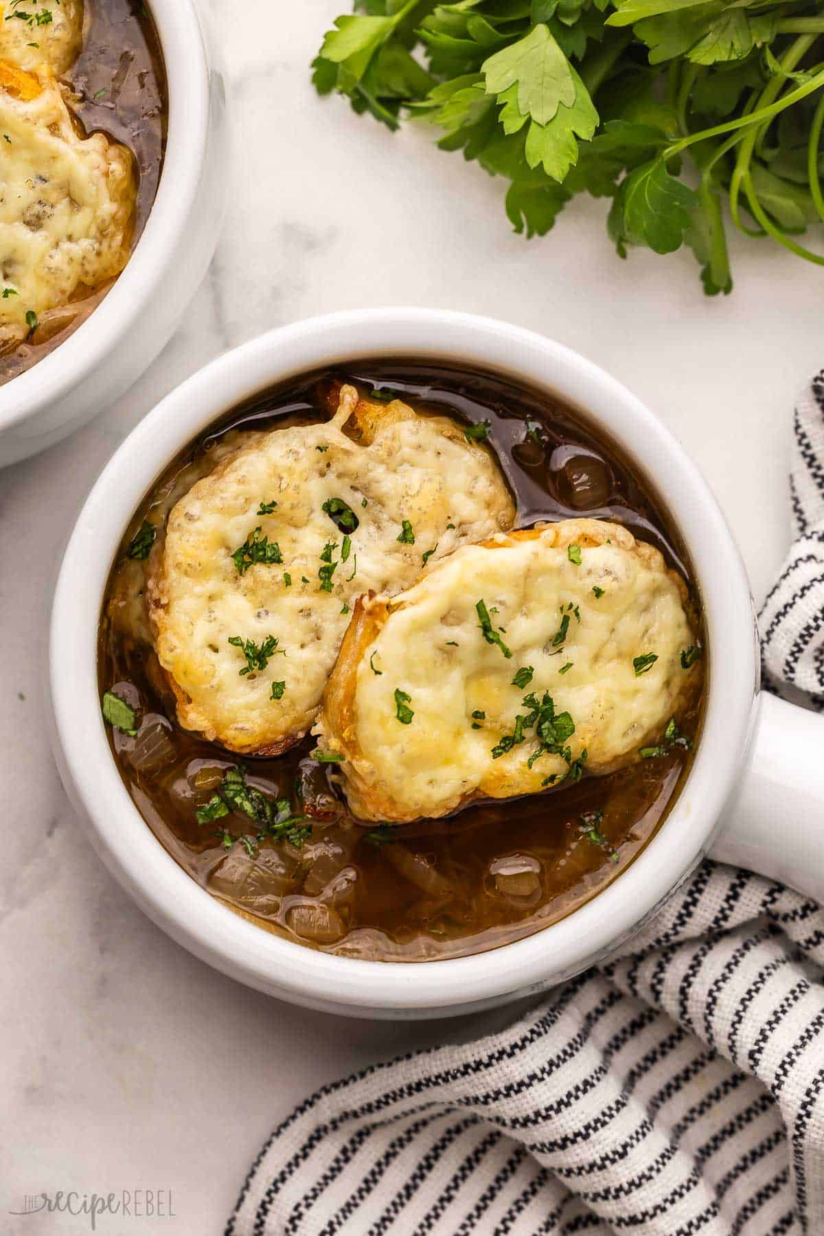 This Slow Cooker French Onion Soup is loaded with caramelized onions, a rich broth, and topped with crusty bread and melty cheese! It's just like the classic version with a more hands-off approach for busy days. #soup #recipe #dinner | slow cooker soup | crockpot soup | slow cooker recipes | comfort food | easy dinner ideas large white bowl of french onion soup with a towel beside.