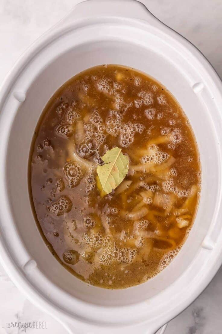 white slow cooker with a bay leaf floating on top of soup.