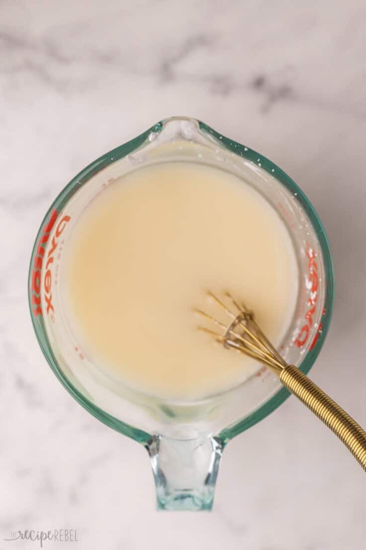 glass measuring cup filled with cream and whisk.