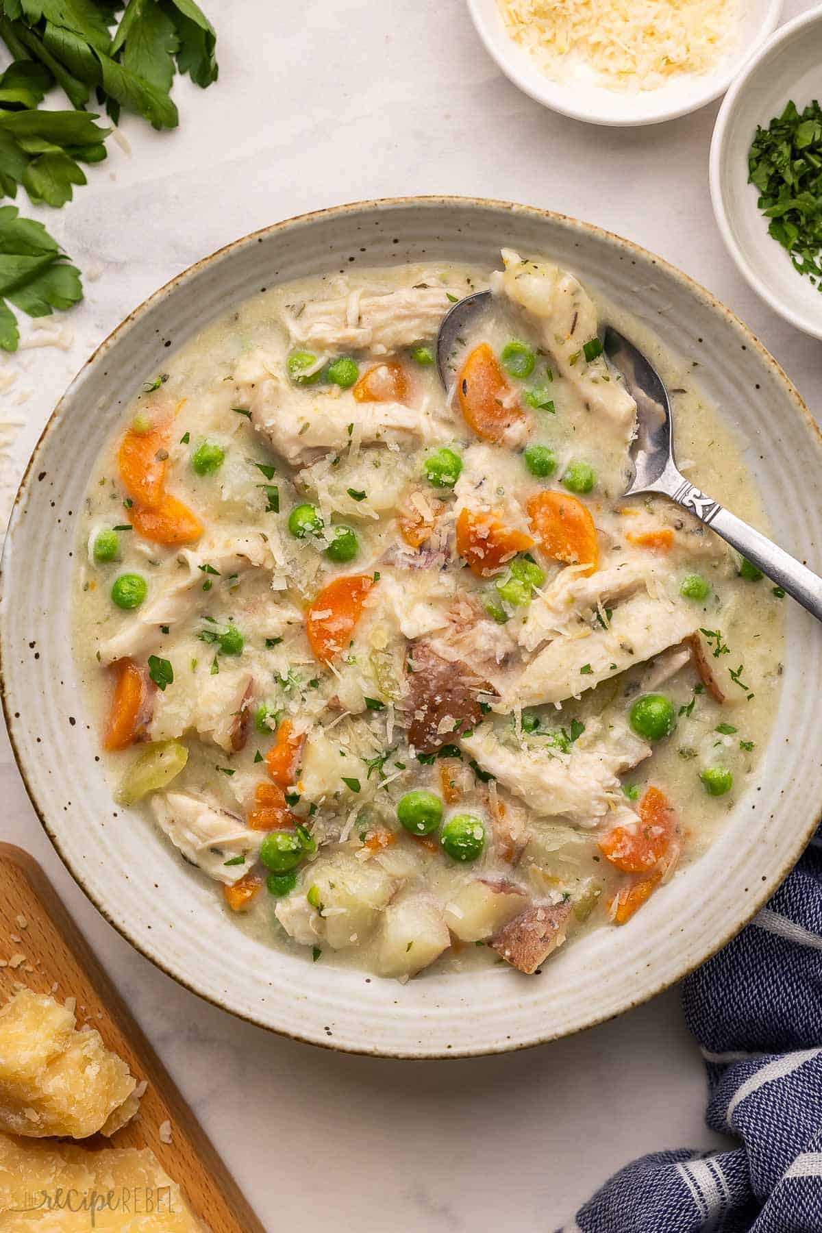 This Slow Cooker Garlic Parmesan Chicken Stew is made with chicken breasts, tender potatoes and vegetables, all simmered in a cheesy, creamy broth! It's the perfect easy crockpot meal to warm you up on a chilly day. #crockpot #slowcooker #dinner | soup recipe | healthy dinner | dinner ideas | chicken dinner ideas | chicken breast | comfort food a speckled bowl full of stew and topped with shredded parmesan.