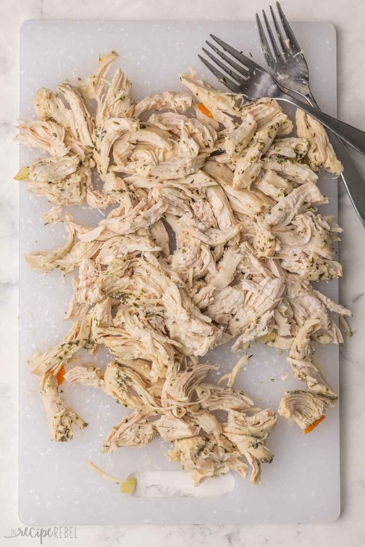 shredded chicken on a white cutting board with forks beside.