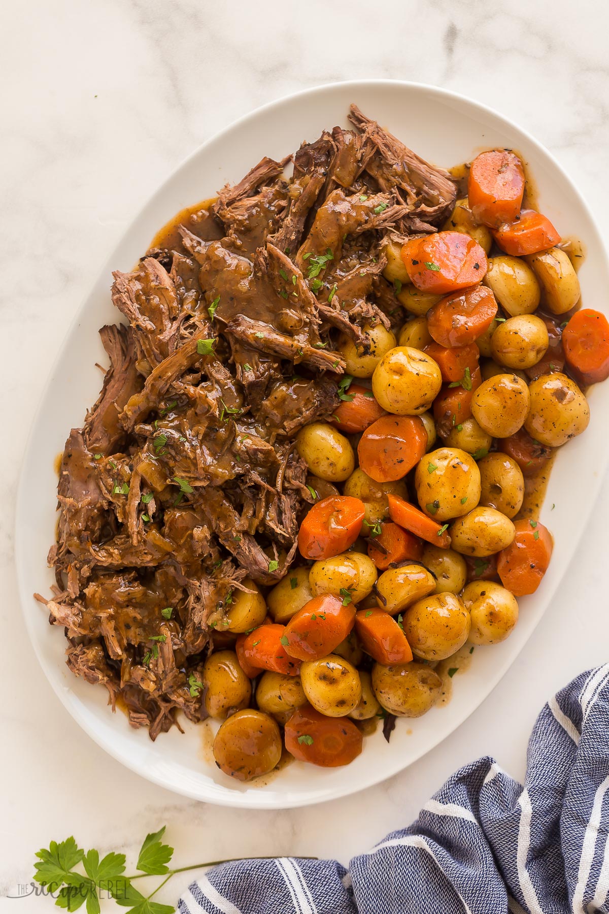 This Slow Cooker Pot Roast has incredible flavor and the best gravy! Creamy potatoes, tender carrots, fall apart roast beef -- it's pure comfort food! #slowcooker #crockpot #recipes | crockpot meals | slow cooker recipes | easy dinner ideas | pot roast recipe | roast beef overhead image of slow cooker pot roast on white platter with a blue towel