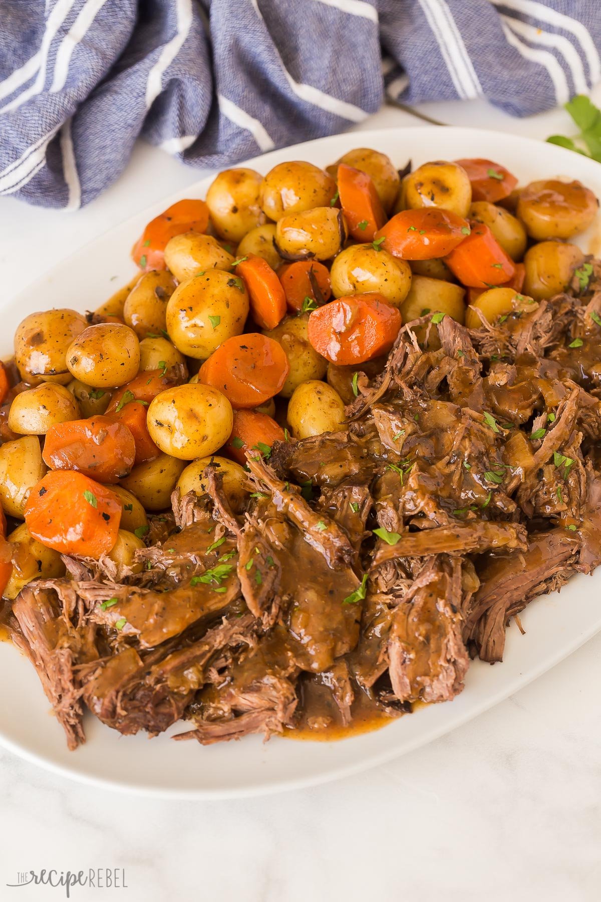 This Slow Cooker Pot Roast has incredible flavor and the best gravy! Creamy potatoes, tender carrots, fall apart roast beef -- it's pure comfort food! #slowcooker #crockpot #recipes | crockpot meals | slow cooker recipes | easy dinner ideas | pot roast recipe | roast beef a platter of crockpot pot roast against a blue towel