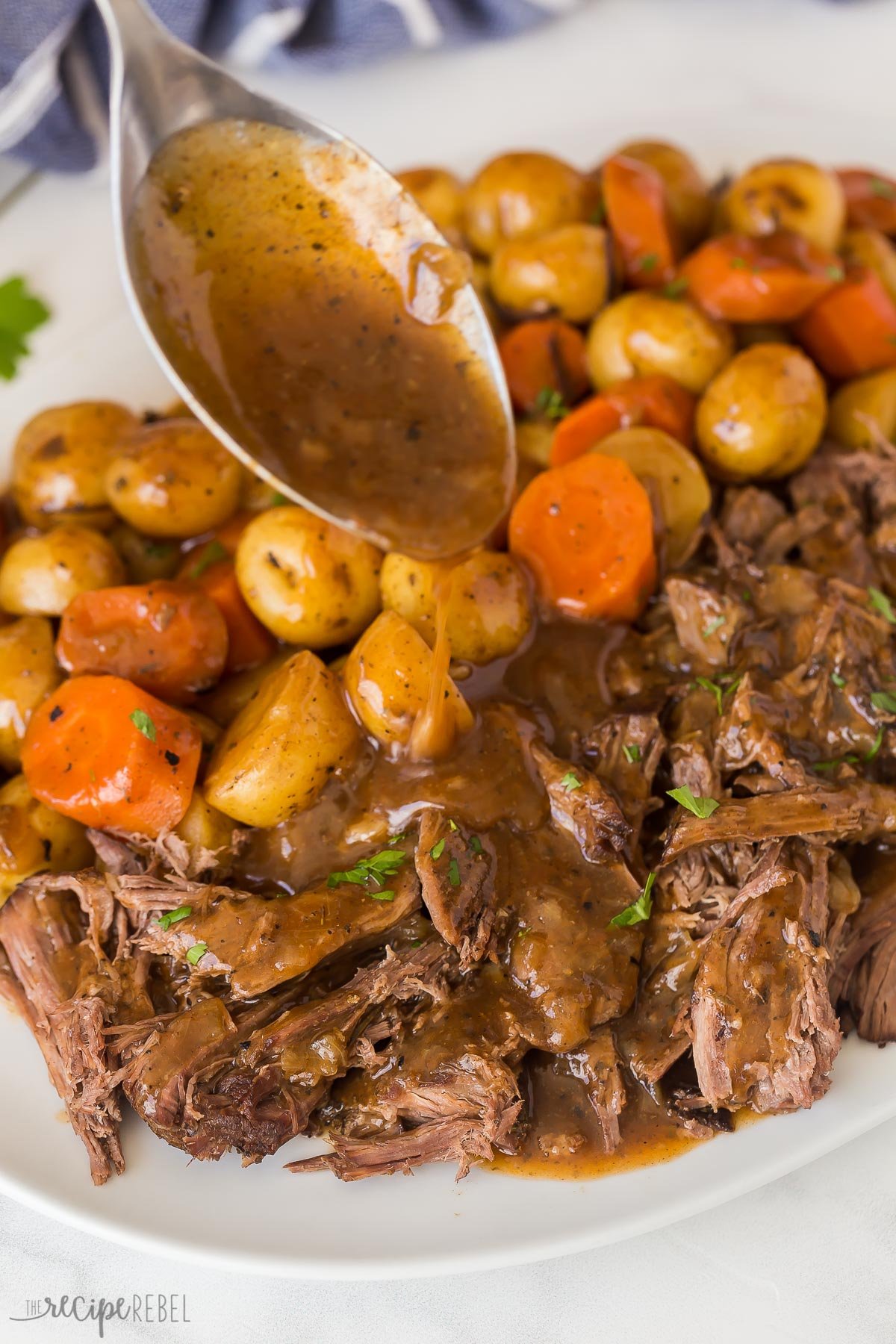 This Slow Cooker Pot Roast has incredible flavor and the best gravy! Creamy potatoes, tender carrots, fall apart roast beef -- it's pure comfort food! #slowcooker #crockpot #recipes | crockpot meals | slow cooker recipes | easy dinner ideas | pot roast recipe | roast beef close up image of gravy being drizzled on slow cooker pot roast