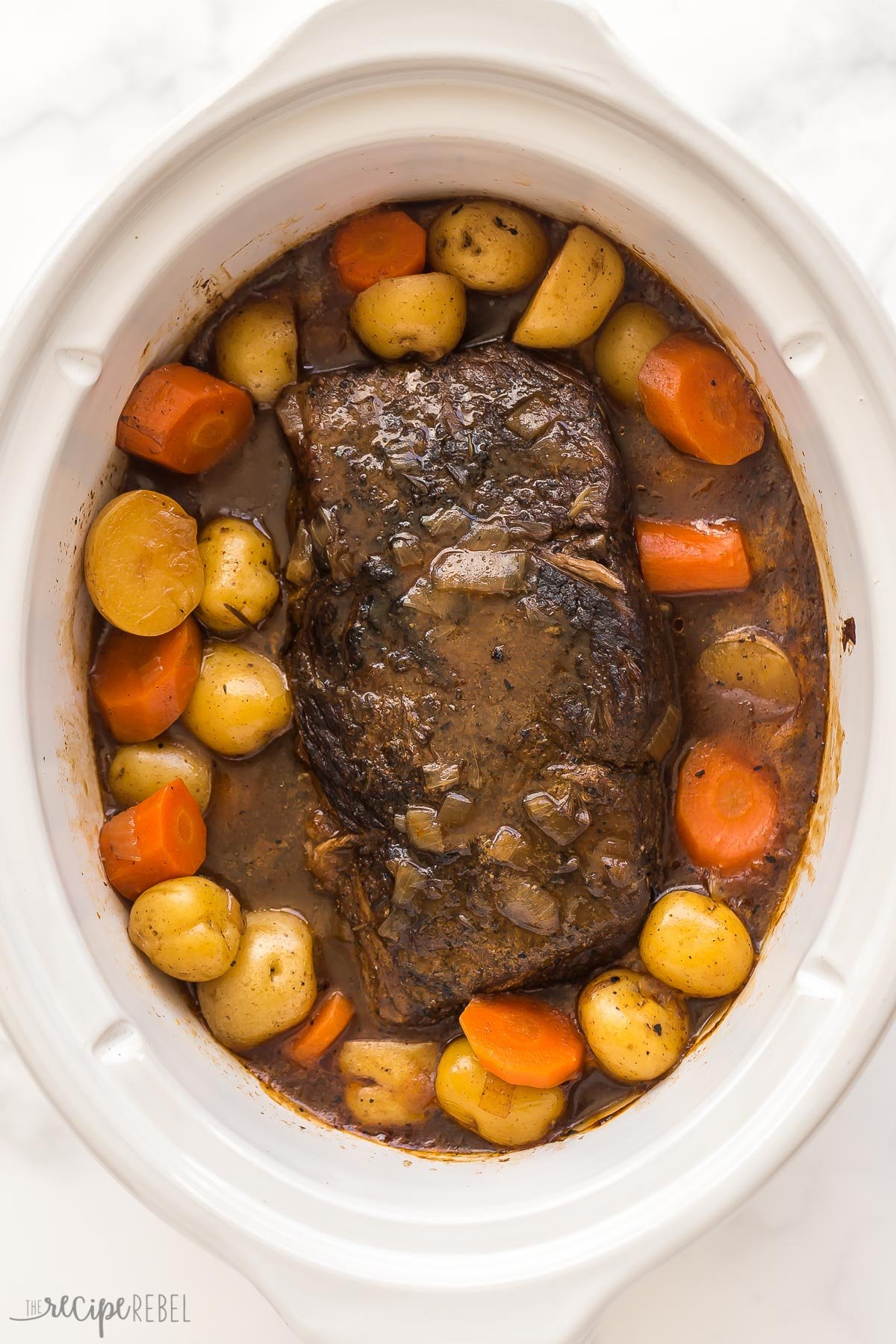 This Slow Cooker Pot Roast has incredible flavor and the best gravy! Creamy potatoes, tender carrots, fall apart roast beef -- it's pure comfort food! #slowcooker #crockpot #recipes | crockpot meals | slow cooker recipes | easy dinner ideas | pot roast recipe | roast beef cooked slow cooker pot roast in white crockpot with potatoes and carrots