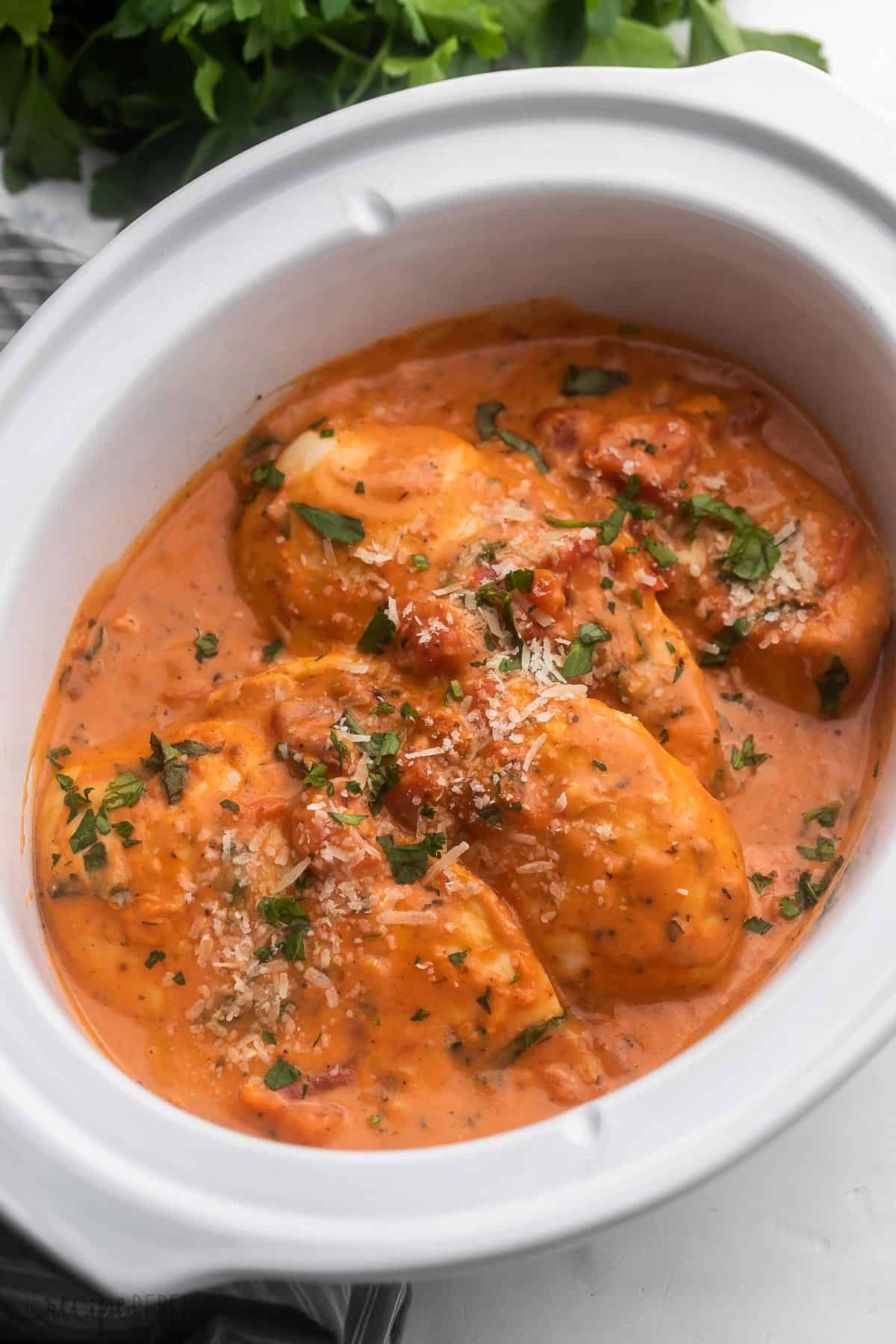 This Slow Cooker Creamy Tomato Basil Chicken Breast is SO easy and flavorful, you wouldn't believe it only has a few ingredients! The perfect easy crockpot chicken recipe for busy weeknights! #chicken #chickenbreast #slowcooker #crockpot #dinner side angle of crockpot chicken breast in tomato basil sauce.