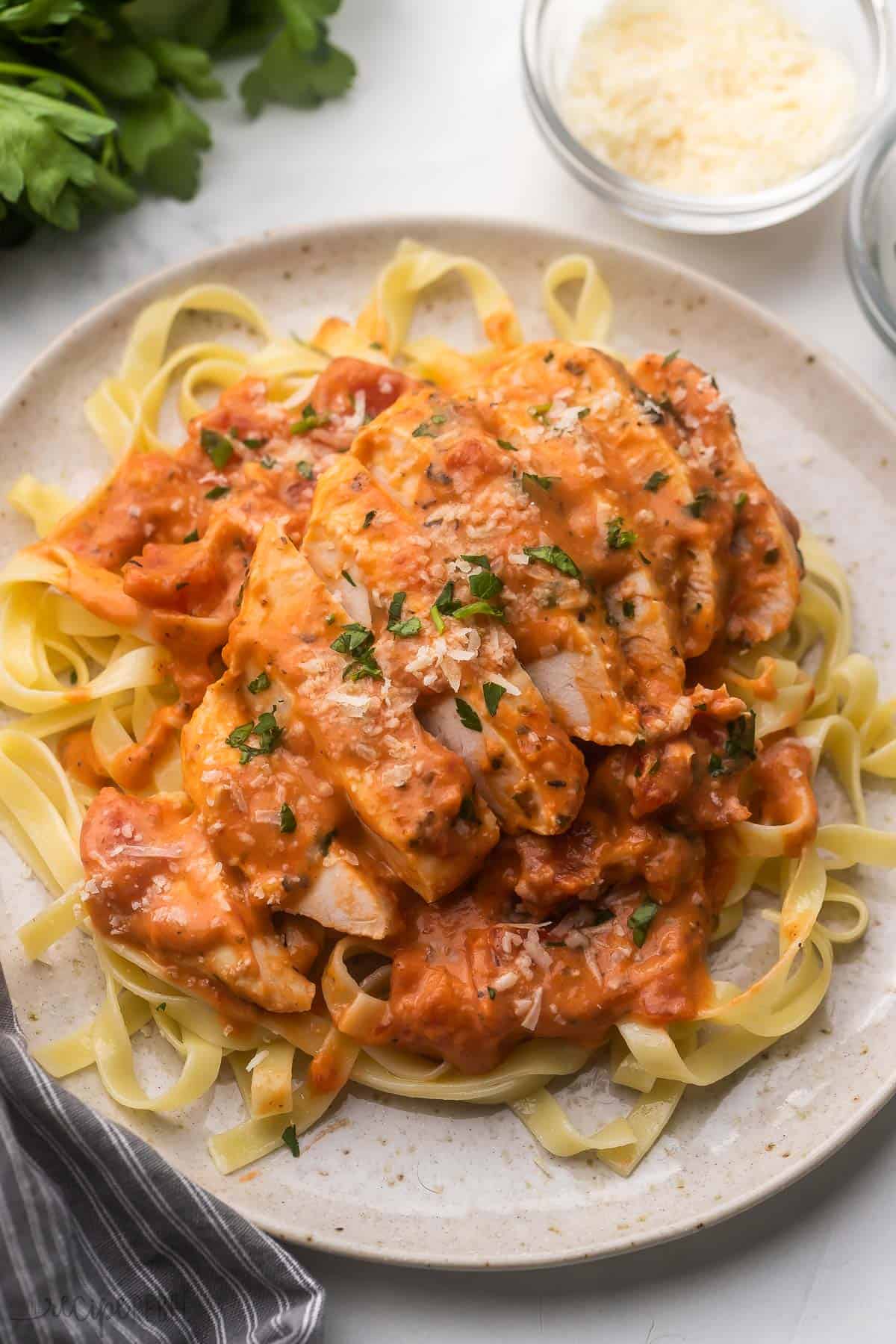 This Slow Cooker Creamy Tomato Basil Chicken Breast is SO easy and flavorful, you wouldn't believe it only has a few ingredients! The perfect easy crockpot chicken recipe for busy weeknights! #chicken #chickenbreast #slowcooker #crockpot #dinner sliced tomato basil slow cooker chicken breast on a plate of pasta.