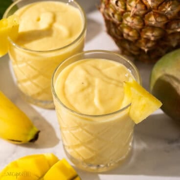 glasses of tropical smoothie with pineapple and mango beside.